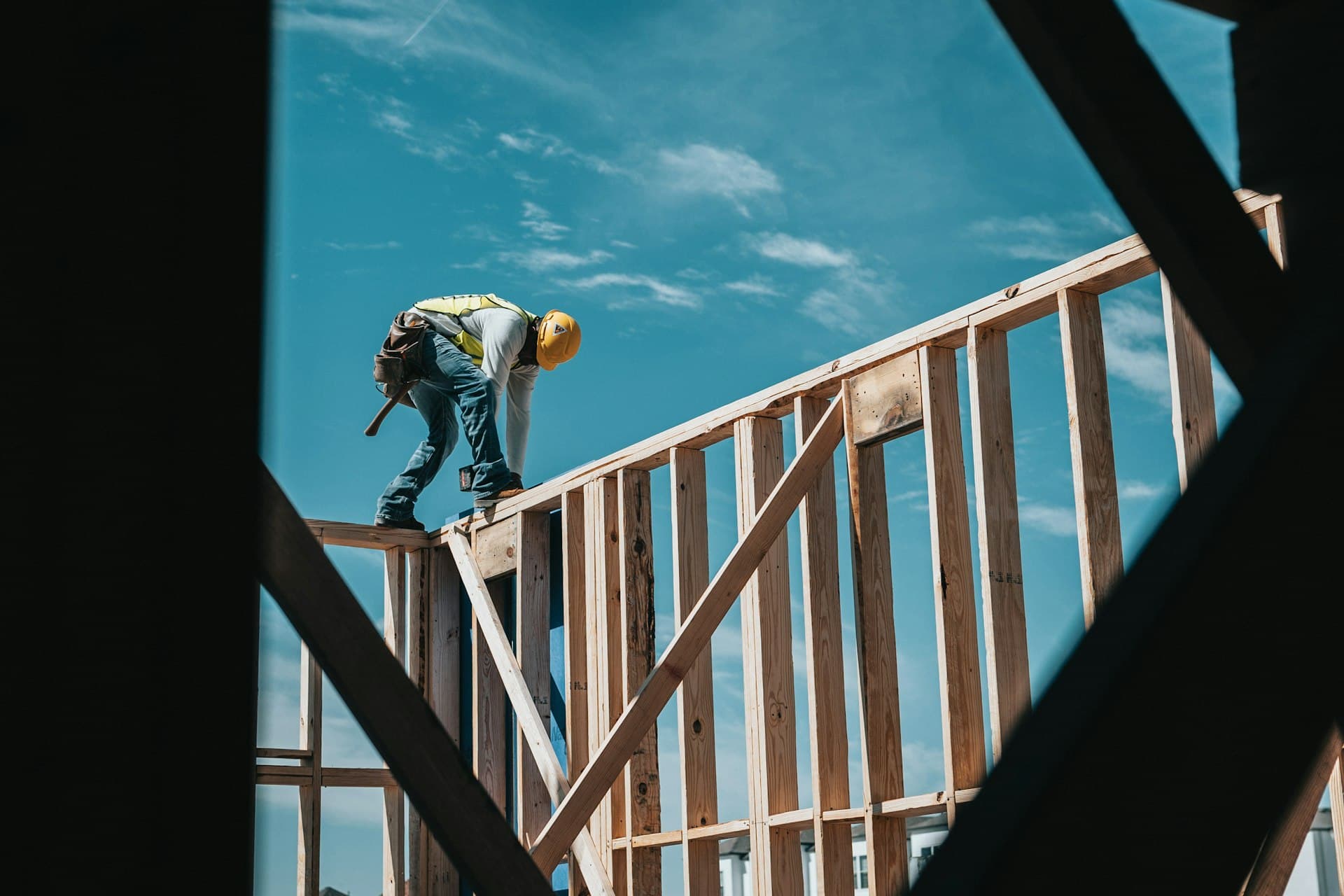 A tradesperson working on a timber-framed build against a clear blue sky